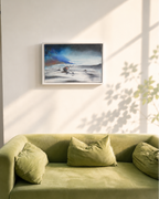 A framed landscape painting hangs on a light beige wall above a green velvet sofa with matching pillows, styled in a sunlit room with soft window shadows.