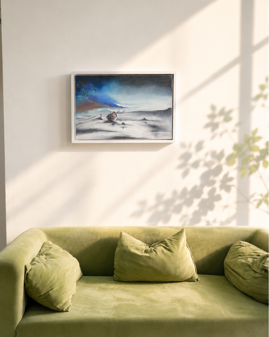A framed landscape painting hangs on a light beige wall above a green velvet sofa with matching pillows, styled in a sunlit room with soft window shadows.