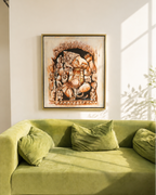A framed art print depicting a detailed Ganesha illustration in warm earthy tones, hanging on a white wall above a green velvet sofa with pillows.